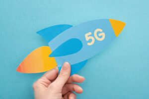 cropped view of woman holding paper rocket with 5g lettering on blue background