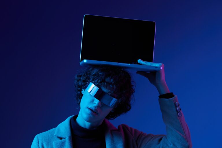 Portrait of a stylish male hacker with a laptop and futuristic glasses in blue light, Blue Perennial